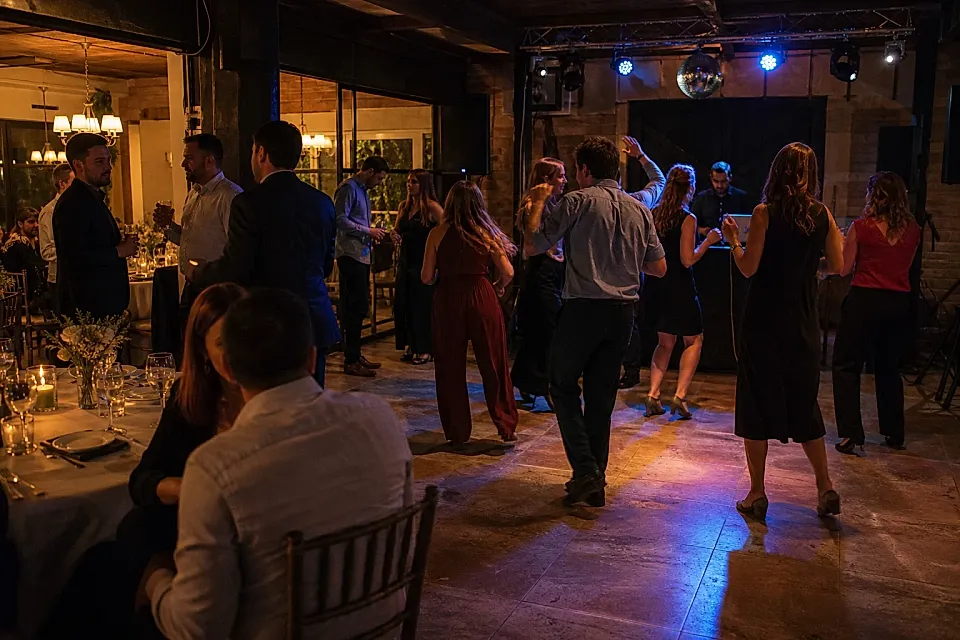 Invitados conversan y bailan en una fiesta nocturna dentro de un salón