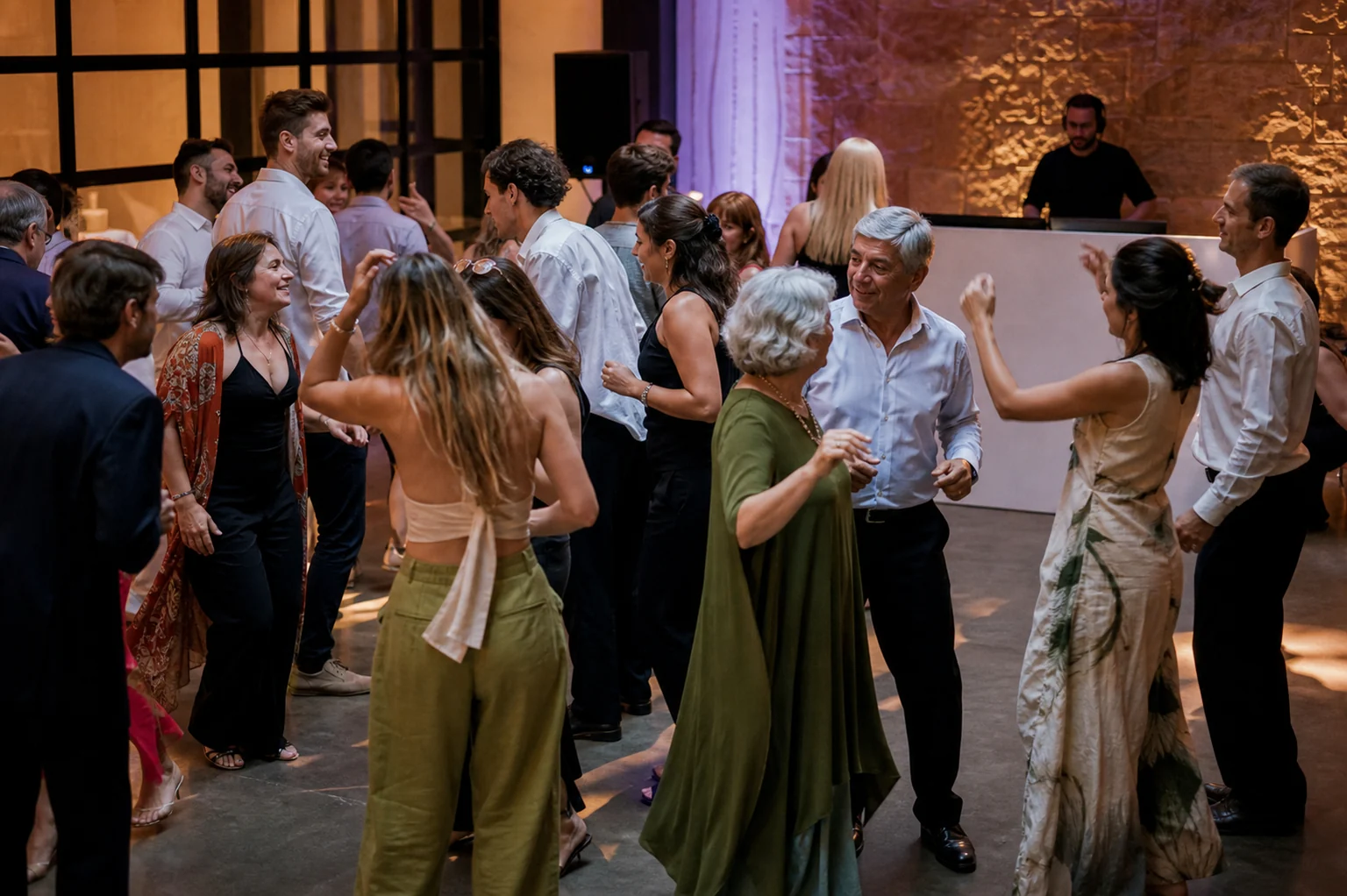 Invitados de distintas edades bailando mientras el DJ observa la pista