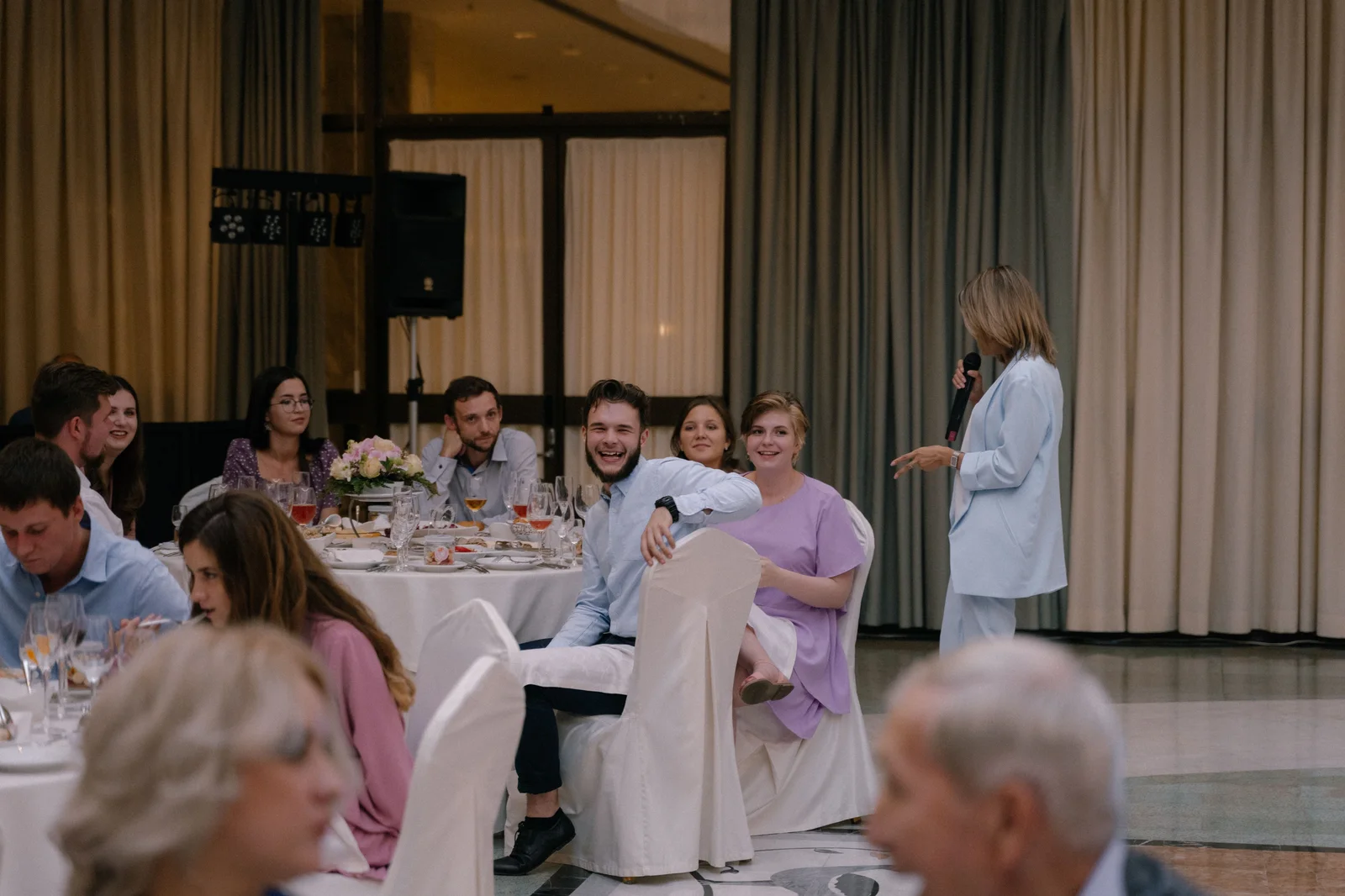 Invitados sentados en mesas escuchan y se ríen durante una recepción