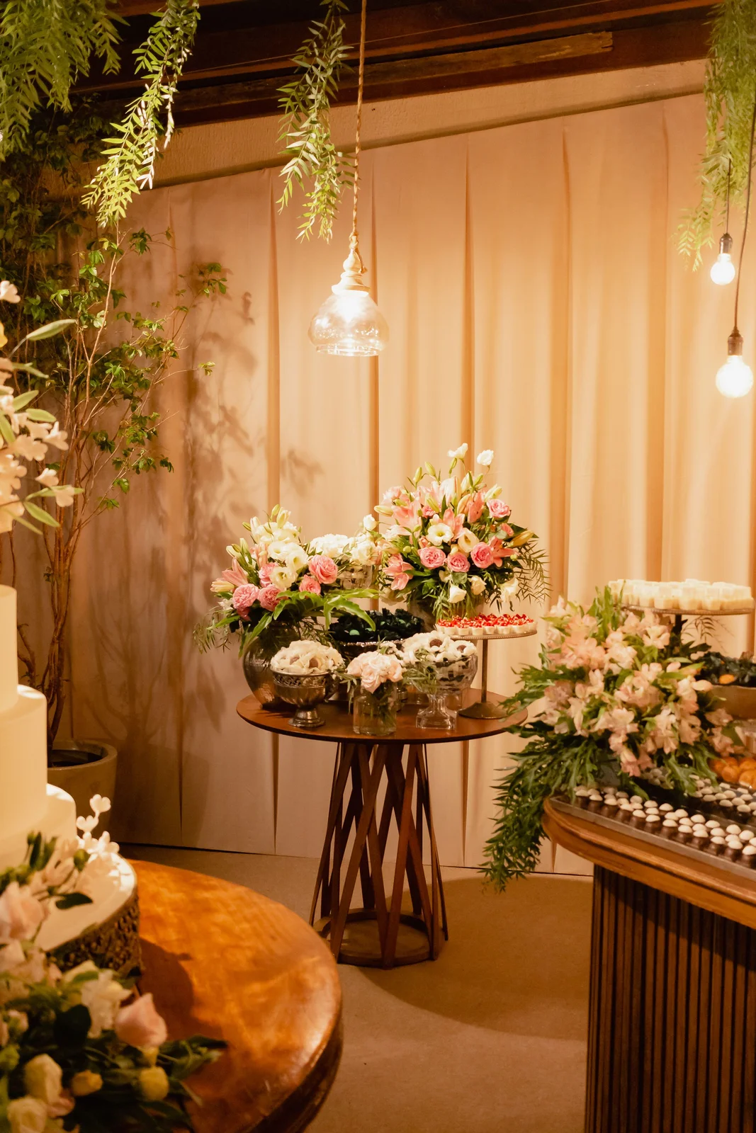 Arreglos de flores rosadas y blancas junto a una mesa dulce iluminada