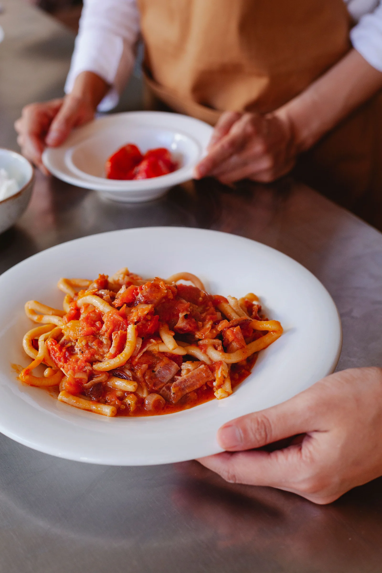 Manos que sostienen dos platos de pasta con salsa de tomate