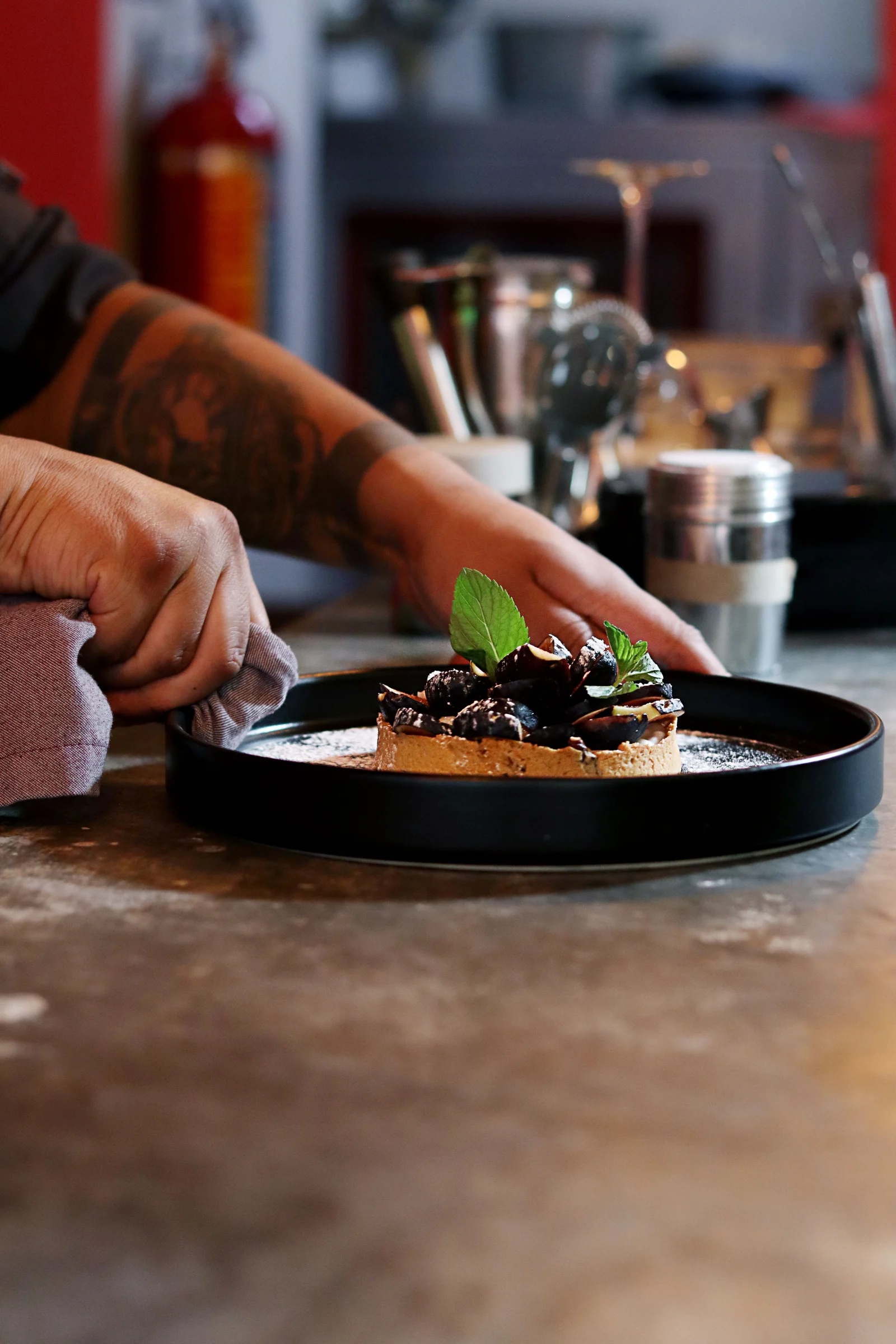 Manos junto a una tarta individual con fruta y hojas de menta en un plato negro