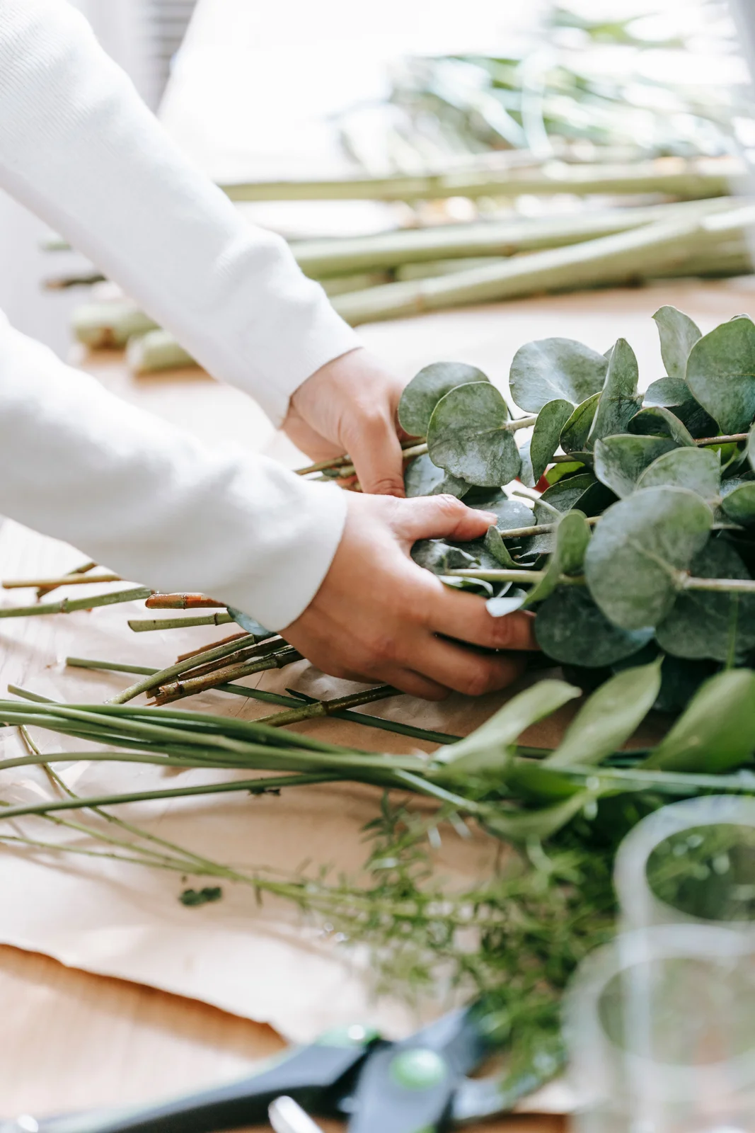 Manos de florista ordenando tallos y ramas de eucalipto sobre una mesa
