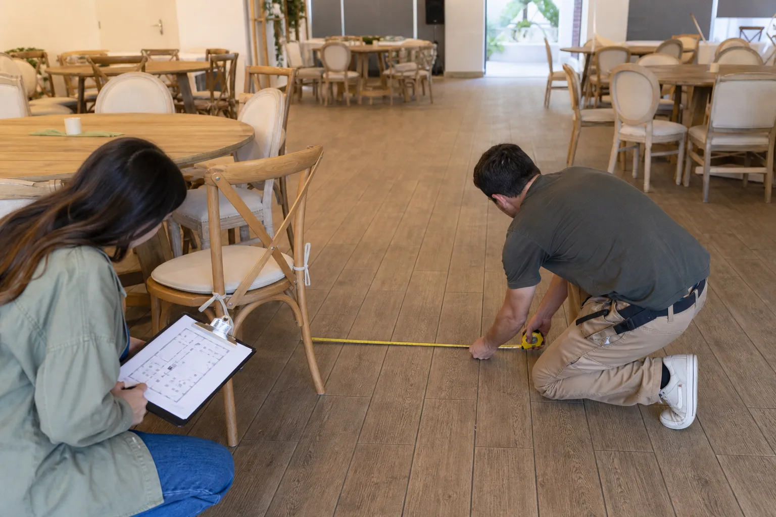 Equipo mide la circulación entre una silla y las mesas mientras revisa el plano del salón