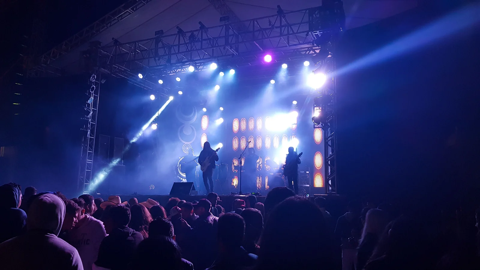 Banda en un escenario iluminado vista desde un público numeroso.