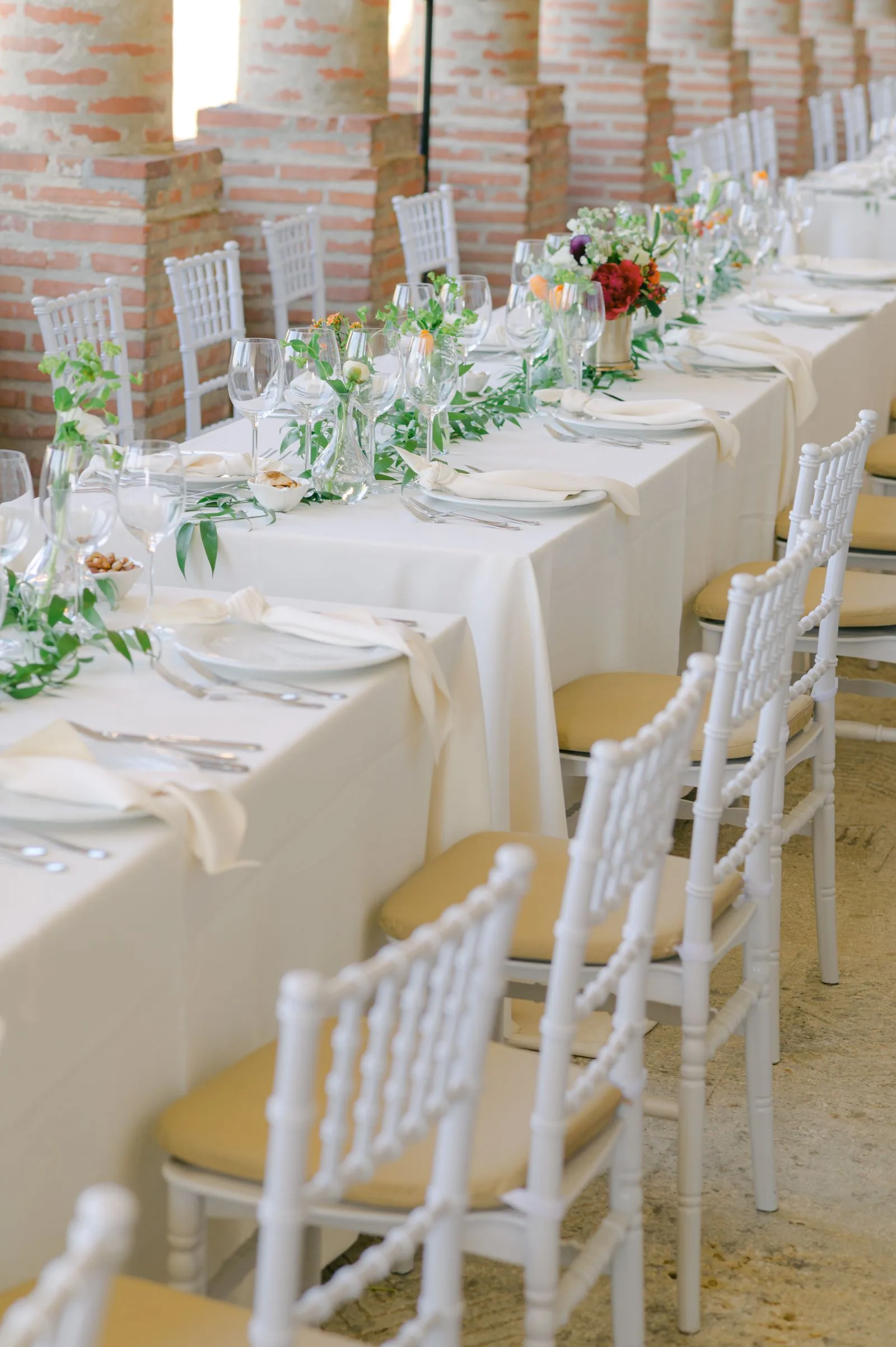 Mesa larga de casamiento con sillas blancas, flores y copas
