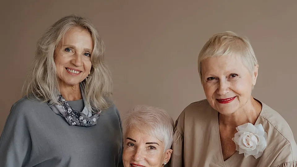 Tres mujeres mayores sonríen juntas durante una celebración.