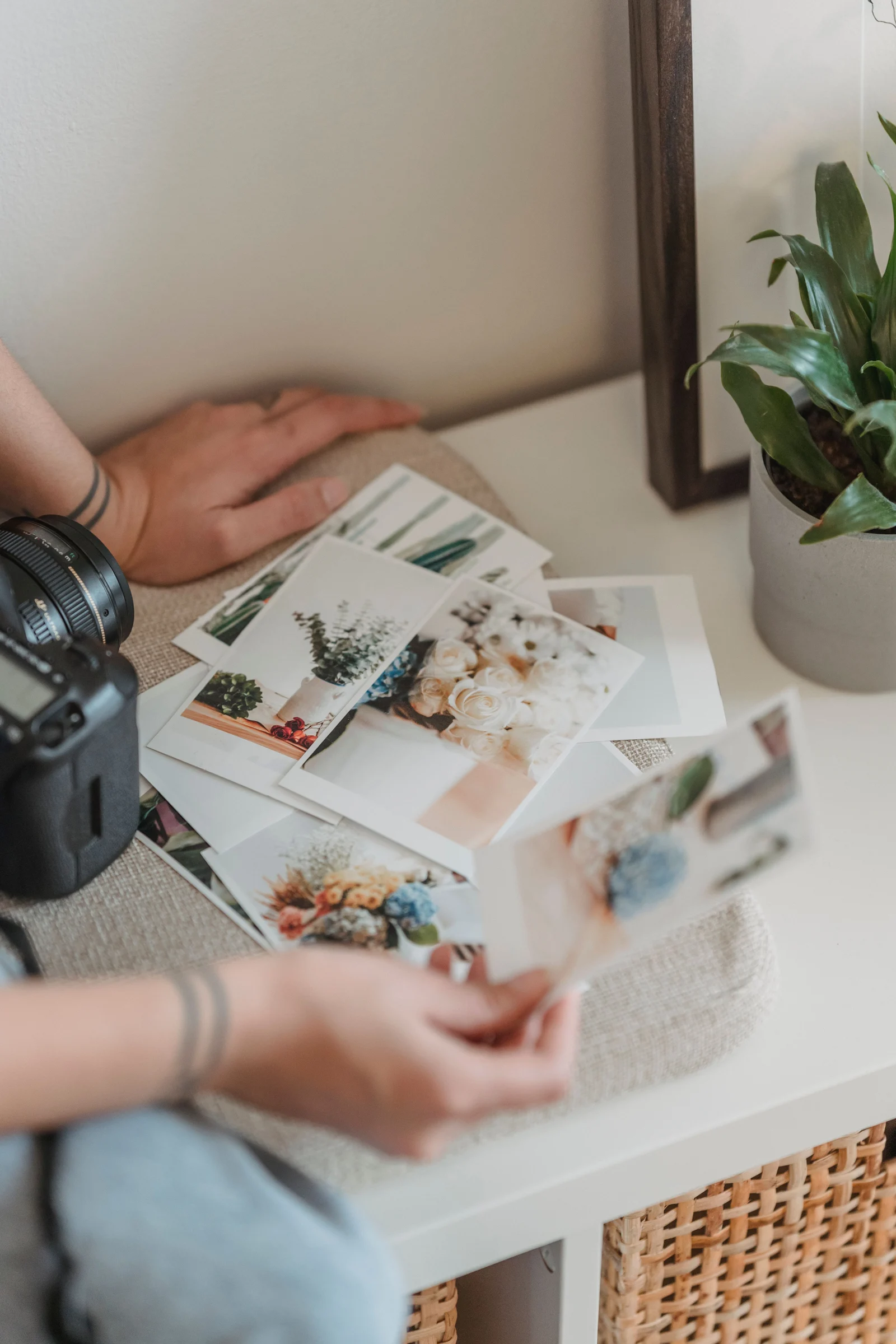 Manos revisando fotografías impresas de flores junto a una cámara.